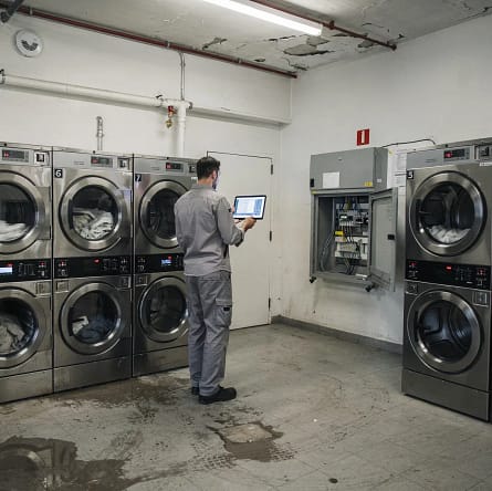 Tecnico controlla da remoto una lavanderia self-service automatica con lavatrici, asciugatrici e impianti di sicurezza visibili